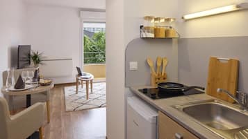 Een moderne keuken met een inbouwvaatwasser, een spoelbak en een aanrecht met een koekenpan. Er is een eethoek met een tafel gedekt voor twee personen en een kleine plant.
