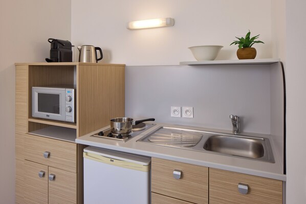 A compact kitchenette with a microwave, stove, sink, and wooden cabinets. - Quality Aparthotel Orléans Sud Zenith (Olivet)