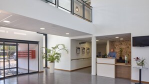 Moderne receptionsområde med receptionist, stor potteplante og et fladskærms-tv på væggen.