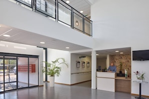 A modern reception area with a receptionist, a large potted plant, and a flat-screen TV on the wall.