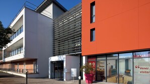 Un bâtiment moderne avec une entrée en verre, une façade rouge et une enseigne sur laquelle on peut lire : « Bienvenue, visiteur ».