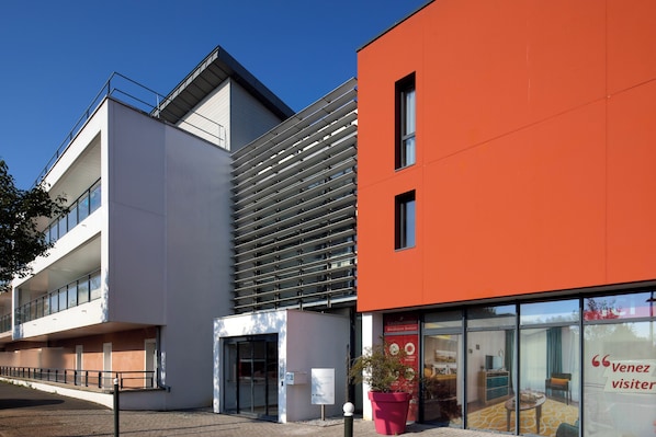 A modern building with a glass entrance, a red facade, and a sign that reads "Venez visiteur".