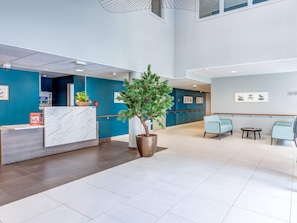 A modern reception area with a marble counter, a potted tree, and light blue seating. - Quality Aparthotel St-Quentin en Yvelines (Montigny-le-Bretonneux)