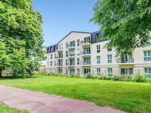 A multi-story residential building with balconies, surrounded by lush greenery and a paved pathway. - Quality Aparthotel St-Quentin en Yvelines (Montigny-le-Bretonneux)