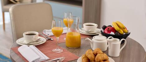 A breakfast table with croissants, juice, coffee, and a fruit basket.