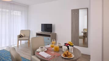 Une chambre d’hôtel avec une table à manger mise pour le petit-déjeuner, une télévision, un miroir et une vue sur la pièce.