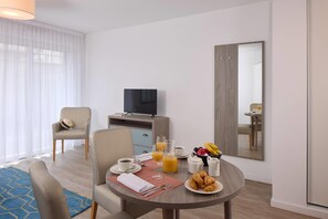 A hotel room with a dining table set for breakfast, a TV, a mirror, and a view of the room. - Quality Aparthotel Morangis Orly (Morangis)