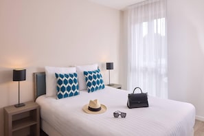 A neatly made bed with patterned pillows, a hat, sunglasses, and a handbag on the bed. - Quality Aparthotel Morangis Orly (Morangis)