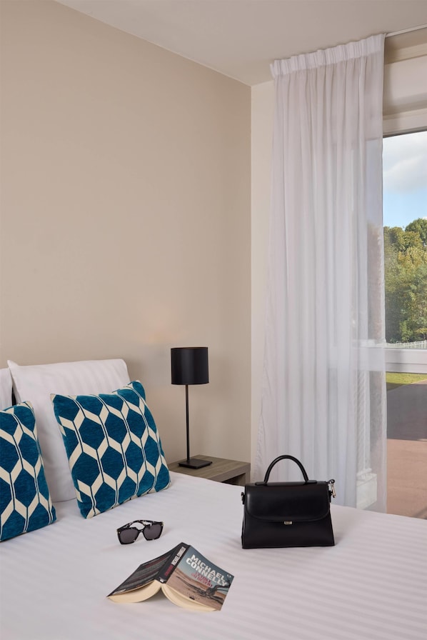 A hotel room with a bed, a black handbag, a pair of sunglasses, and a book on the bed. - Quality Aparthotel Morangis Orly (Morangis)