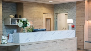 A reception desk with a marble top, wooden paneling on the walls, a vase of flowers, and a lamp. - Quality Aparthotel Morangis Orly (Morangis)