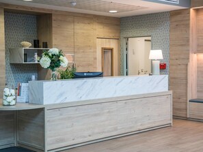 A reception desk with a marble top, wooden paneling on the walls, a vase of flowers, and a lamp. - Quality Aparthotel Morangis Orly (Morangis)
