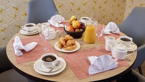 A breakfast setting with croissants, fruit, coffee, and juice on a round table with placemats and napkins. - Quality Aparthotel Morangis Orly (Morangis)