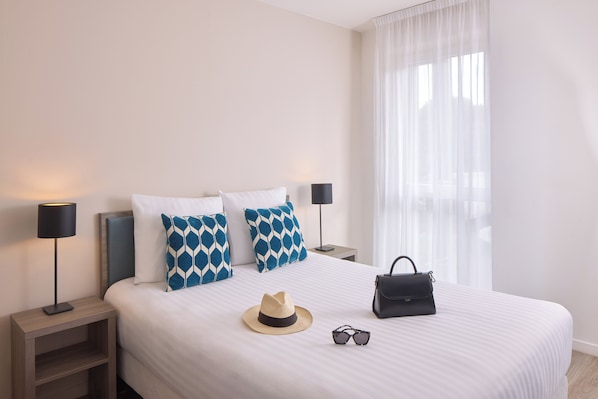 A neatly made bed with patterned pillows, a hat, sunglasses, and a handbag on the bed. - Quality Aparthotel Morangis Orly (Morangis)