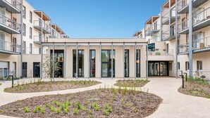 A modern building with multiple balconies, a central courtyard with plants, and a clear sky. - Quality Aparthotel Morangis Orly (Morangis)