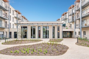 A modern building with multiple balconies, a central courtyard with plants, and a clear sky. - Quality Aparthotel Morangis Orly (Morangis)