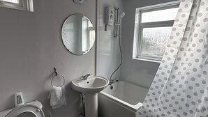 Een badkamer met toilet, wastafel en badkuip. Er is een raam met uitzicht op bomen en een douchegordijn met stippen.