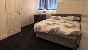 Een slaapkamer met een bed, een nachtkastje, een raam met gordijnen en een deur.