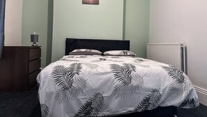 Een slaapkamer met een bed, nachtkastje, lamp en radiator.