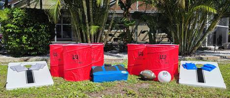 Un área con césped, contenedores de basura rojos identificados como 'WickedBig' y una mesa blanca con una franja negra.