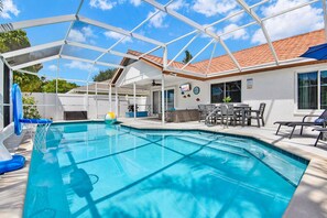 Una piscina con zona cubierta, un patio con asientos y una casa con tejado de baldosas.
