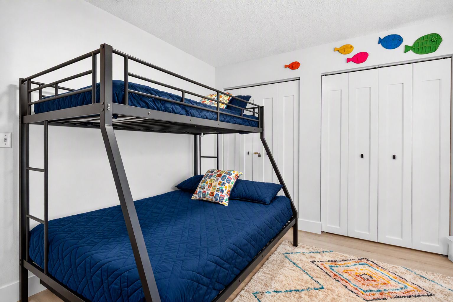 A bunk bed with a blue mattress, a colorful pillow, and a patterned rug on a wooden floor.
