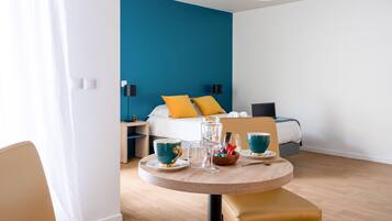 A hotel room with a bed, bedside table, and a round table with cups and a glass.