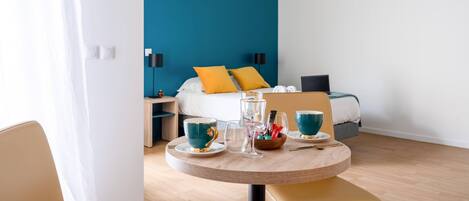 Una habitación de hotel con cama, mesita de noche y una mesa redonda con tazas y un vaso.