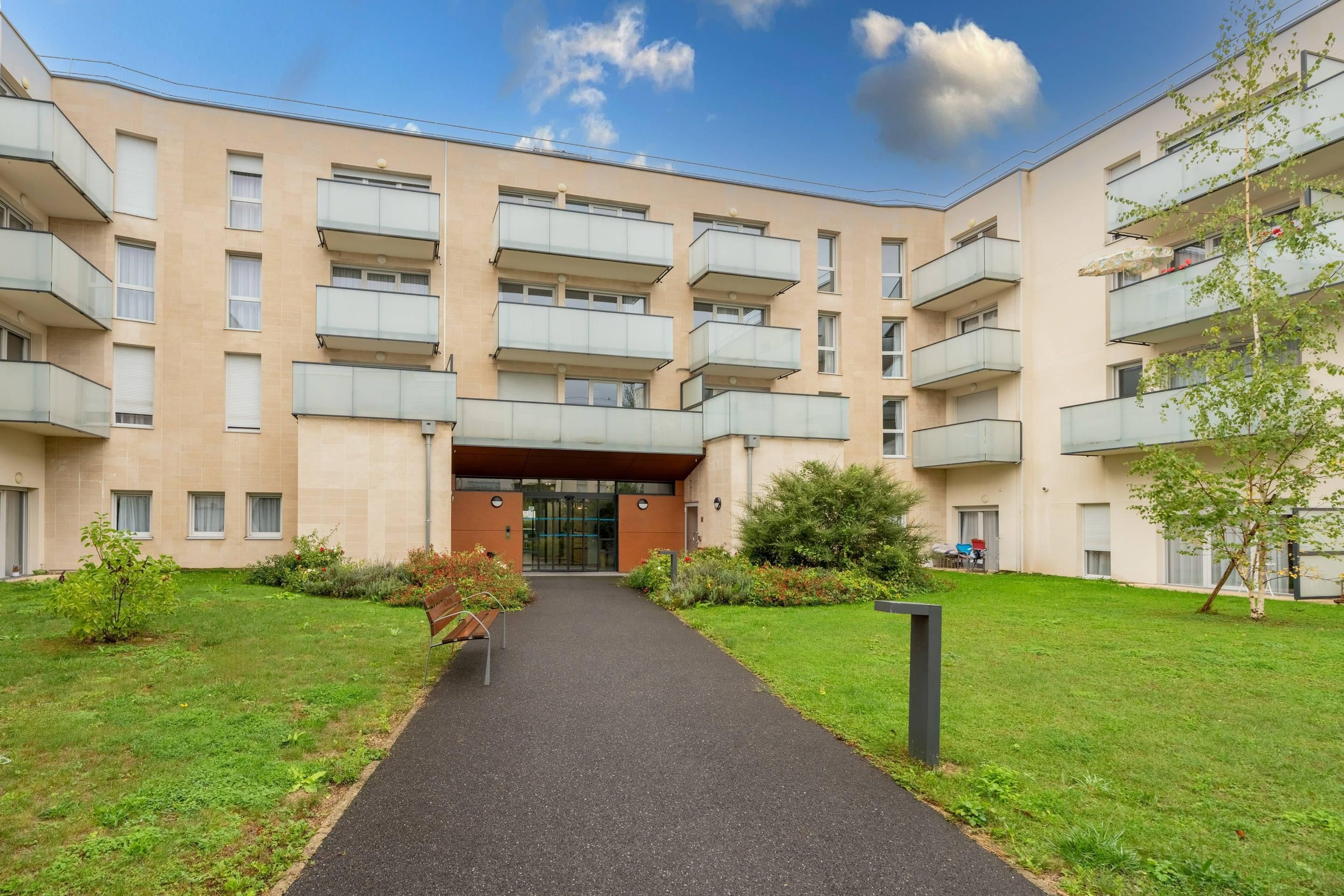 A multi-story residential building with balconies, a central entrance, and a well-maintained lawn.