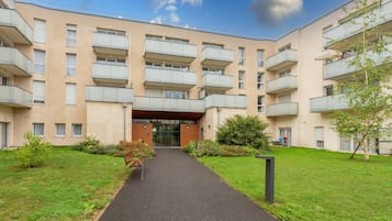 A multi-story residential building with balconies, a central entrance, and a well-maintained lawn.