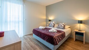 A modern bedroom with a bed, bedside lamps, a nightstand, and a wooden desk. - Quality Aparthotel Reims - Les Capucins (Reims)
