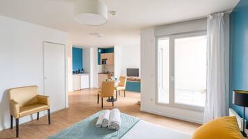 A hotel room with a bed, a sofa, a dining table, and a kitchen in the background.