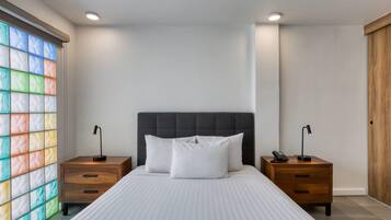 Quarto com cama, duas mesas de cabeceira, um criado-mudo, uma janela com vidro colorido e um guarda-roupa de madeira.