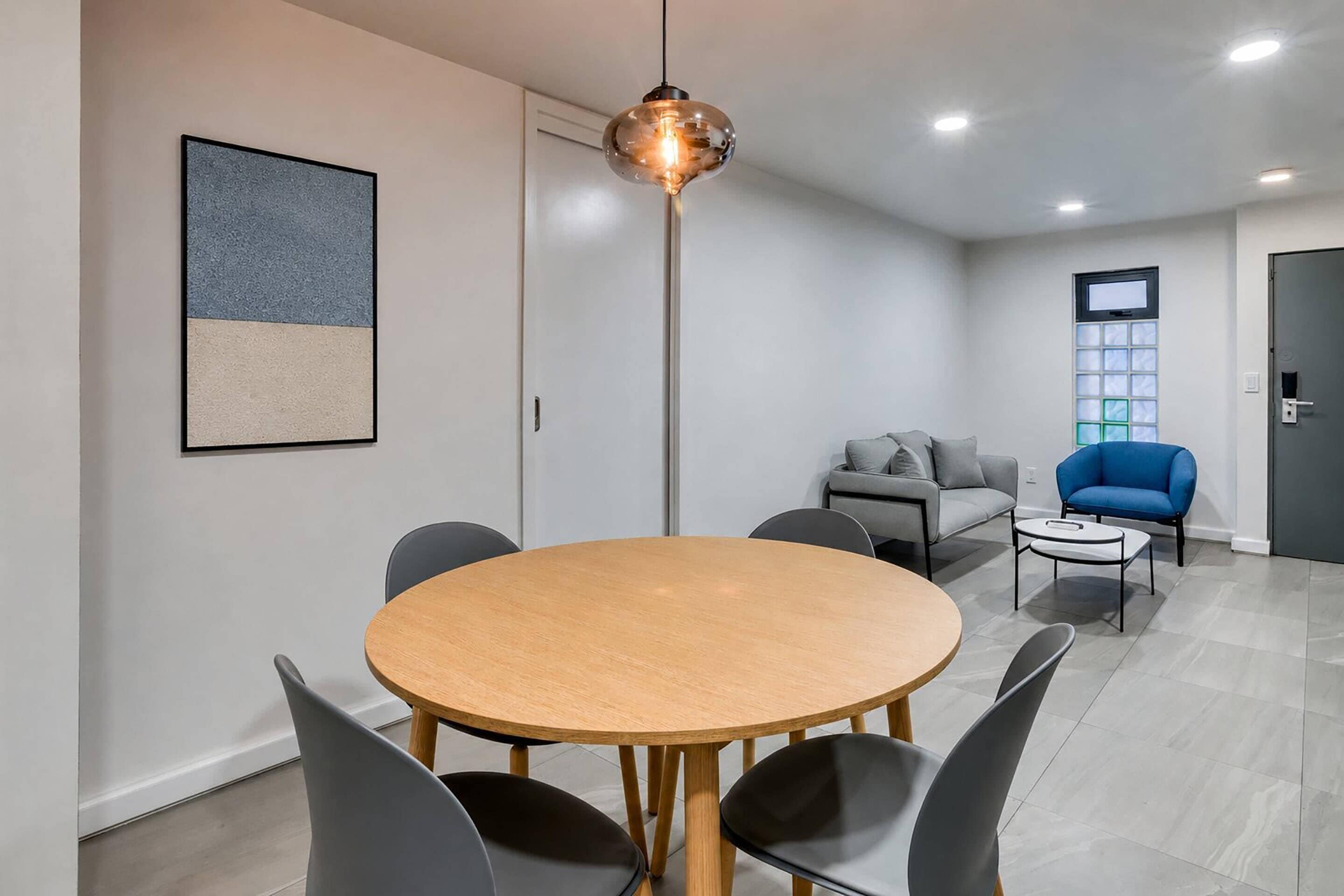 A modern room with a round wooden table, grey chairs, a blue armchair, a grey sofa, and a floor lamp.