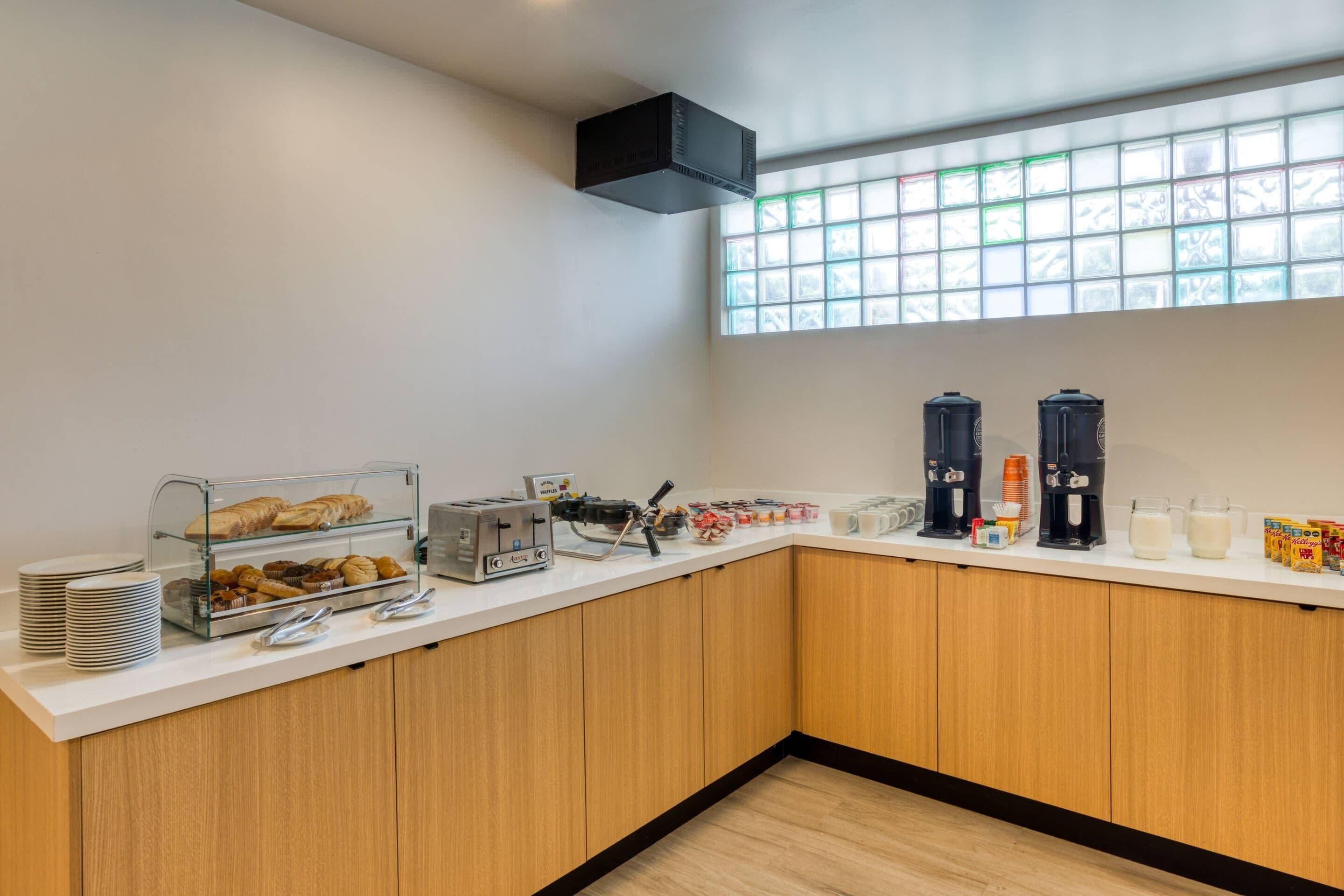 A breakfast bar with pastries, a coffee station, and a window with a grid pattern.