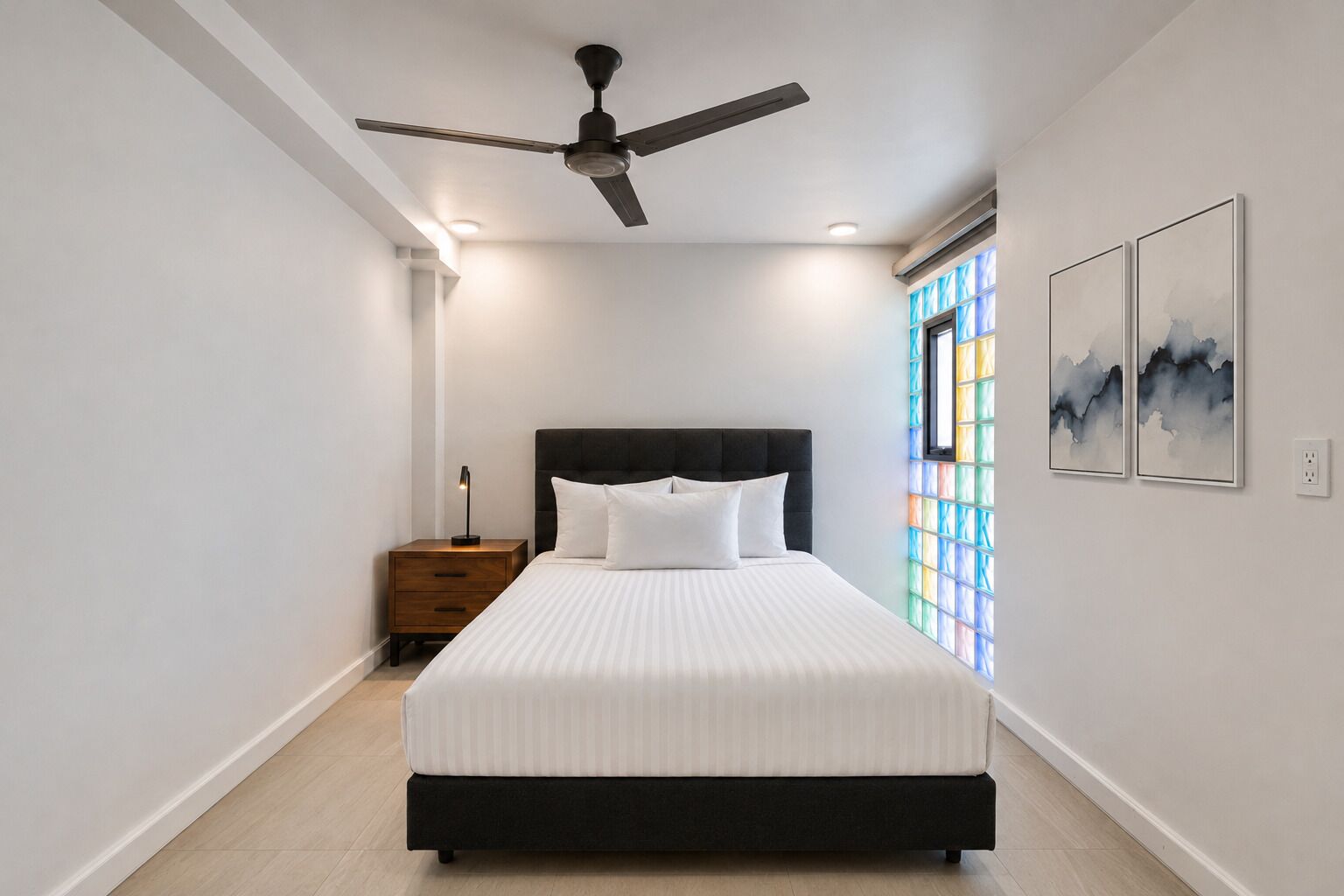 A bedroom with a bed, a nightstand, a ceiling fan, and a window with stained glass.
