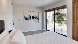 Une chambre d’hôtel moderne avec un grand lit, une porte-fenêtre coulissante donnant sur l’extérieur et deux tableaux abstraits accrochés au mur.