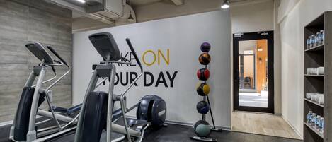A gym with treadmills, a wall with motivational text, a rack of exercise balls, and a water bottle shelf.