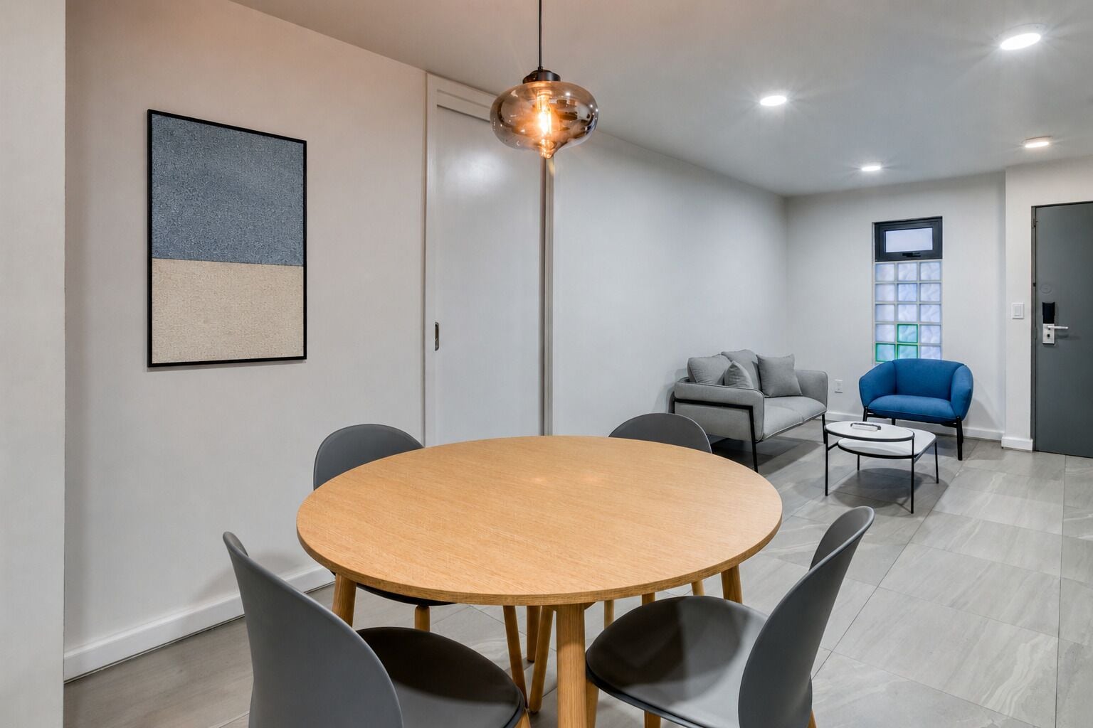 A modern room with a round wooden table, four chairs, a grey sofa, a blue armchair, and a floor lamp.