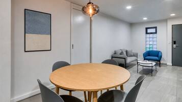 A modern room with a round wooden table, four chairs, a grey sofa, a blue armchair, and a floor lamp.
