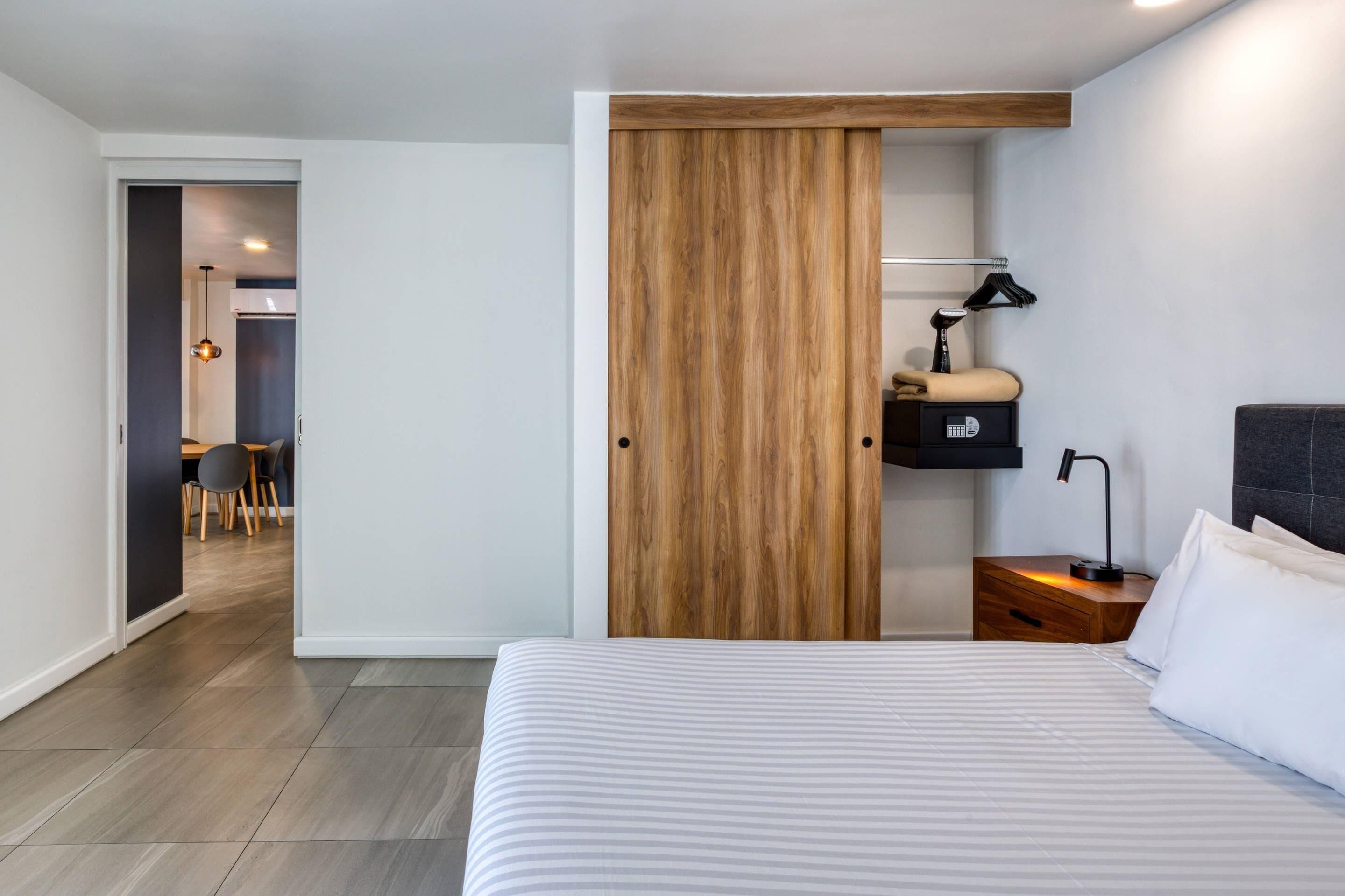 A bedroom with a bed, a wooden wardrobe, a nightstand with a lamp, and a small table with a lamp.