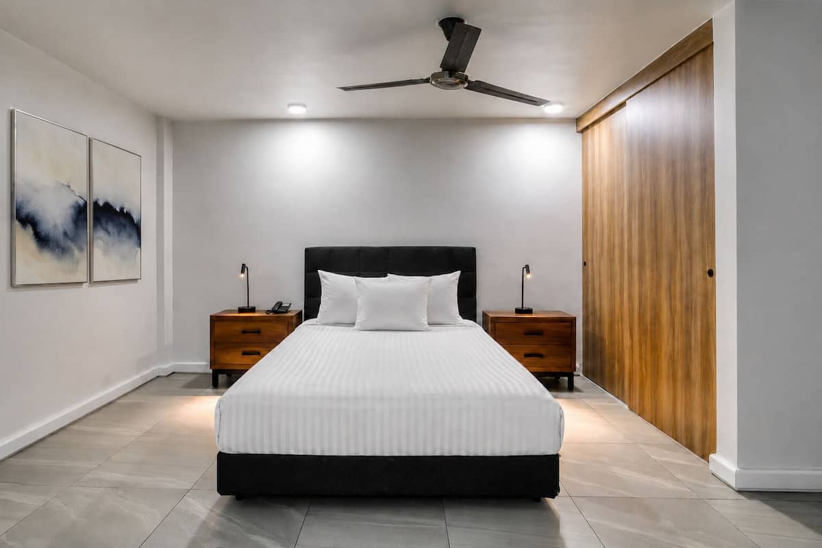 A bedroom with a bed, two bedside tables, a ceiling fan, and a wooden wardrobe.