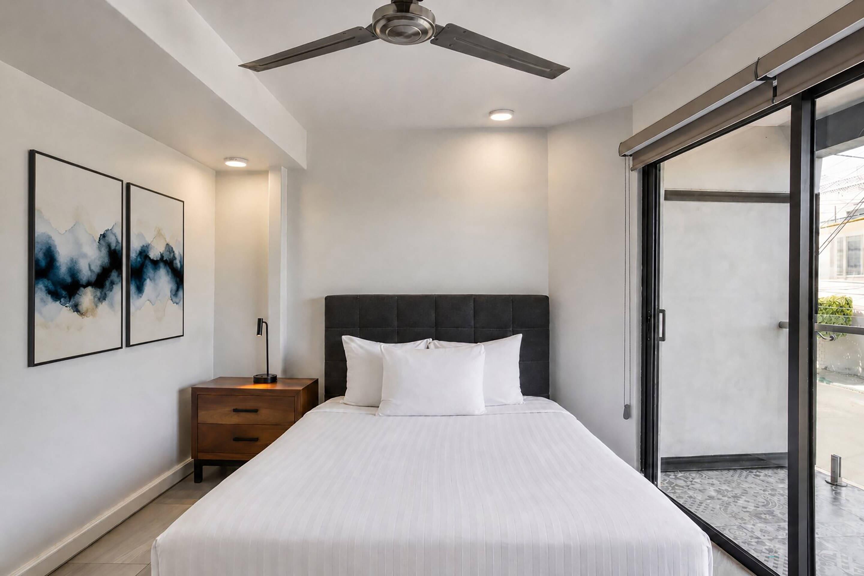 A bedroom with a bed, a nightstand, a ceiling fan, and a large window.