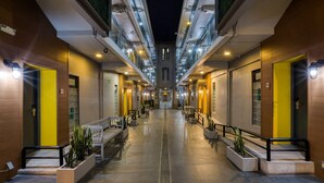 Un couloir d’hôtel avec une allée centrale, des bancs, des jardinières et un design architectural moderne.