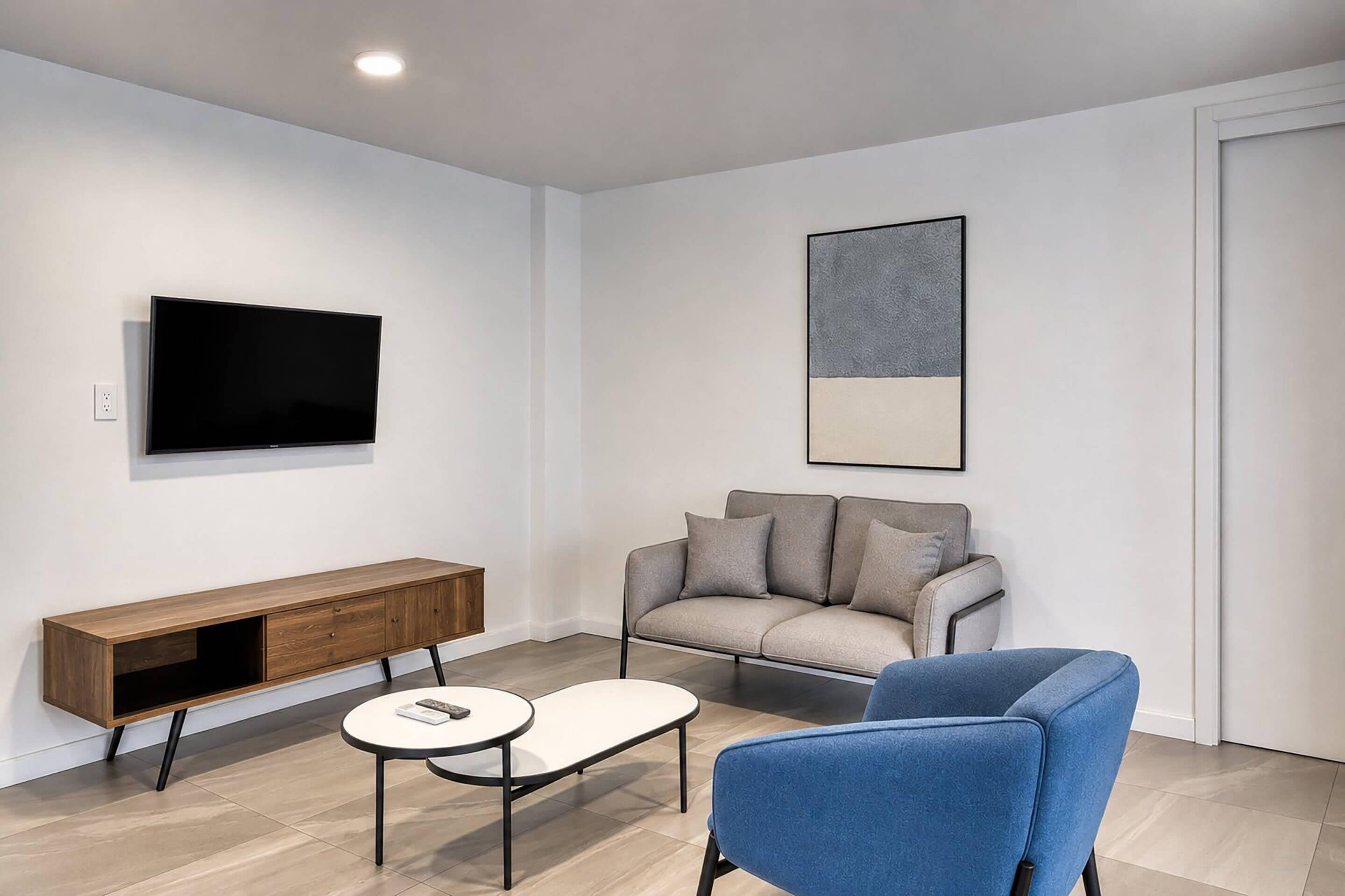 Una sala de estar moderna con un sofá, un sillón azul, una mesa de centro y un televisor montado en la pared.