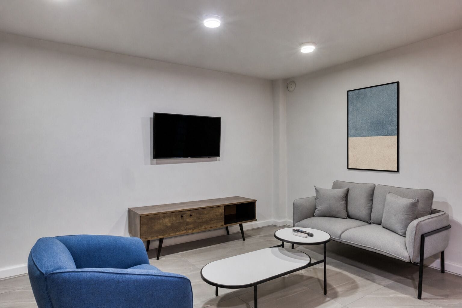 Una sala de estar moderna con un sofá, un sillón azul, una mesa de centro, un televisor y un mueble consola minimalista.