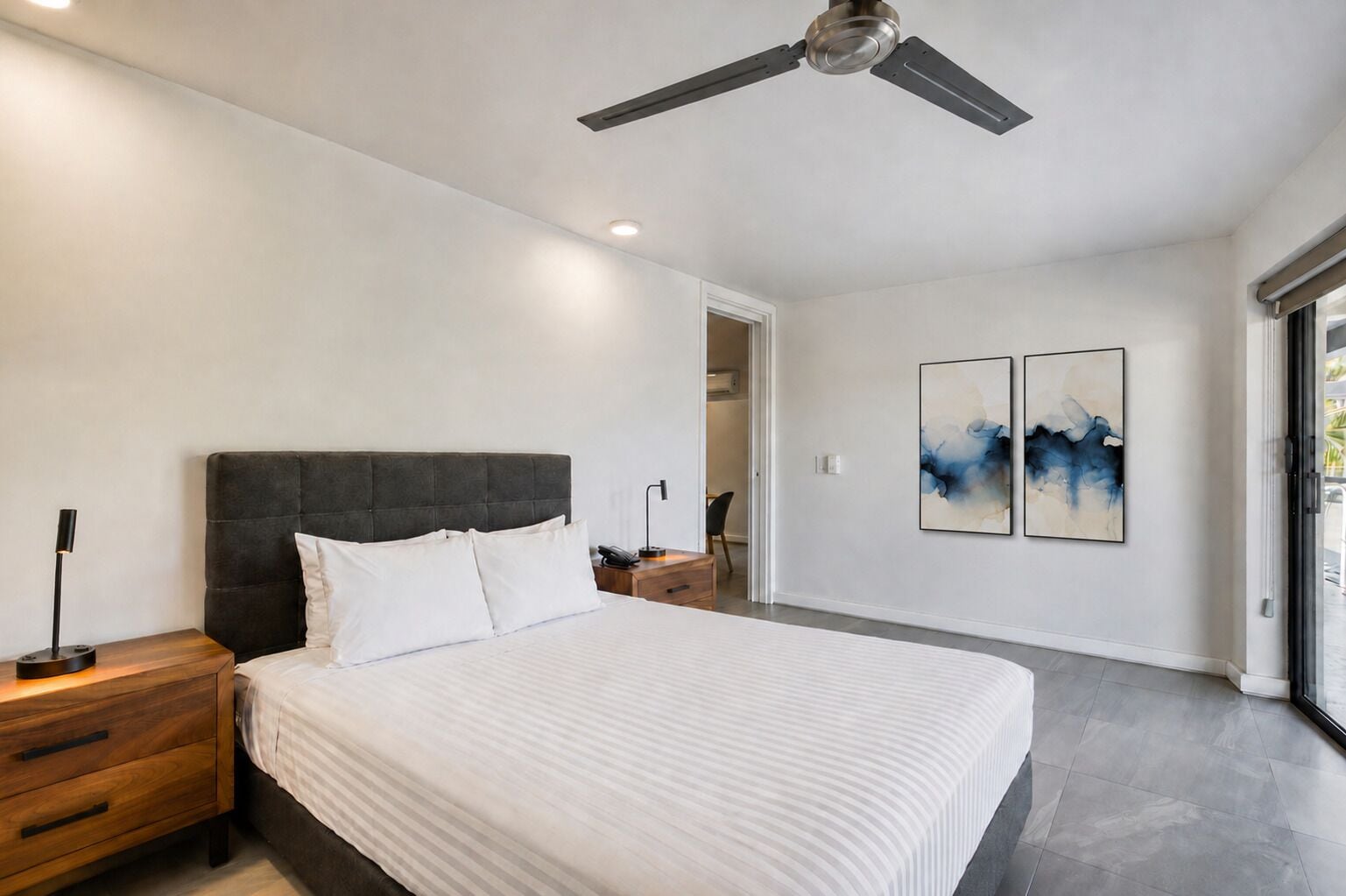 Una camera da letto moderna con un letto, comodini, una ventola a soffitto e opere d'arte astratte alle pareti.