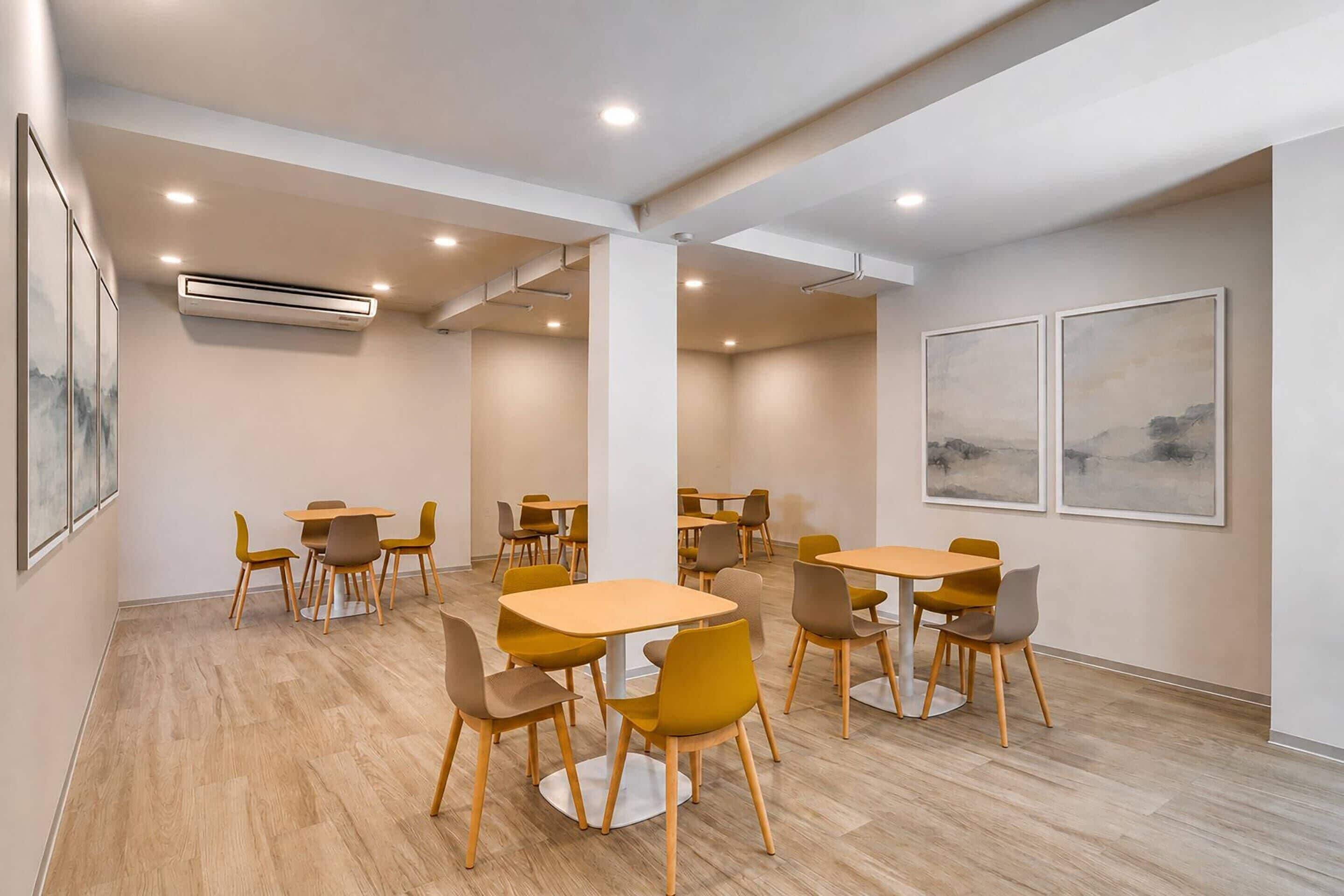 A modern dining area with multiple tables and chairs, recessed ceiling lighting, and artwork on the walls.