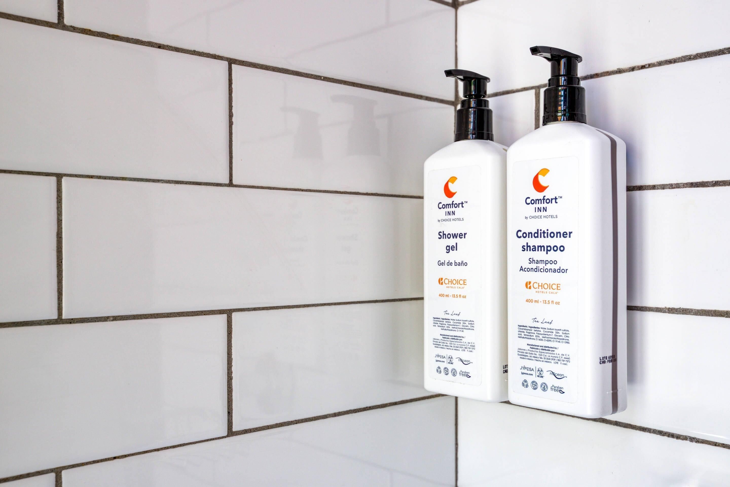 Dos botellas de gel de ducha y acondicionador champú Comfort™ INN by Choice Hotels sobre una pared de azulejos blancos.