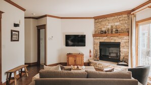 A living room with a stone fireplace, a flat-screen TV, a wooden cabinet, and a bench.