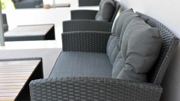 A modern outdoor seating area with a long, dark wicker sofa and matching cushions, a wooden table, and a wicker chair. - LiRi - Family paradise (Ialysos)